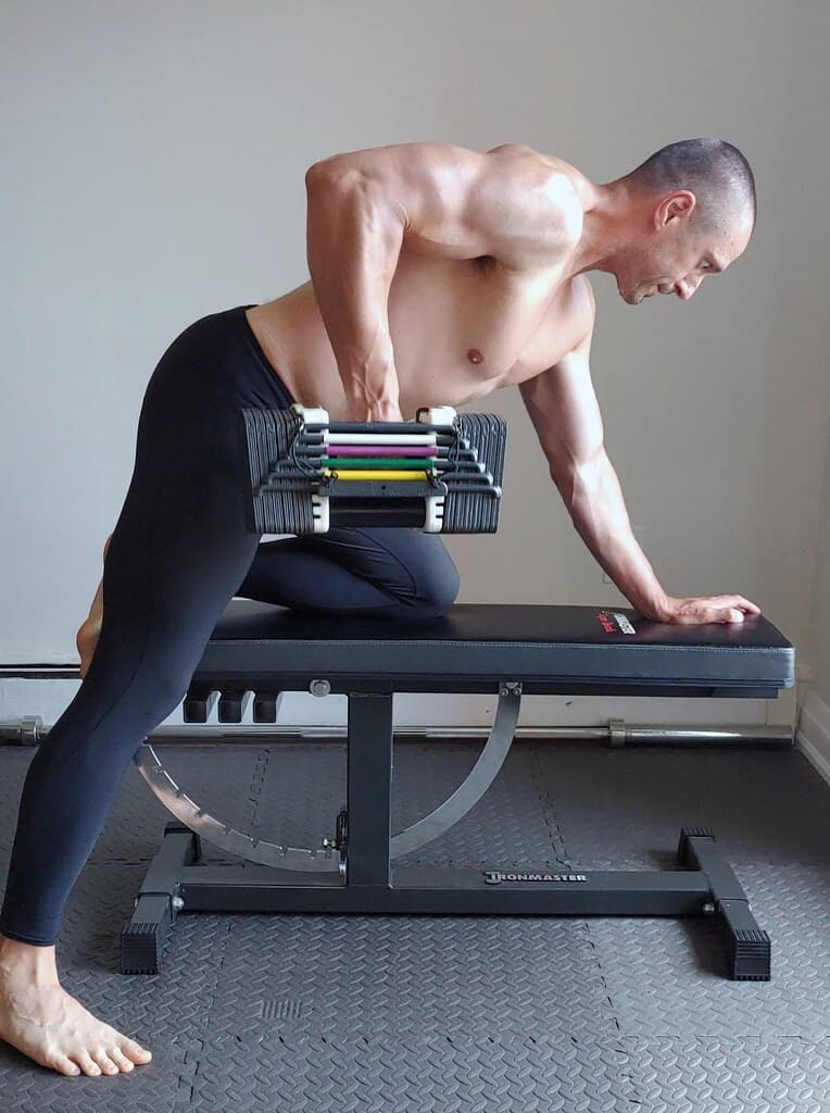 Man doing a dumbbell row on a bench in a compact home gym