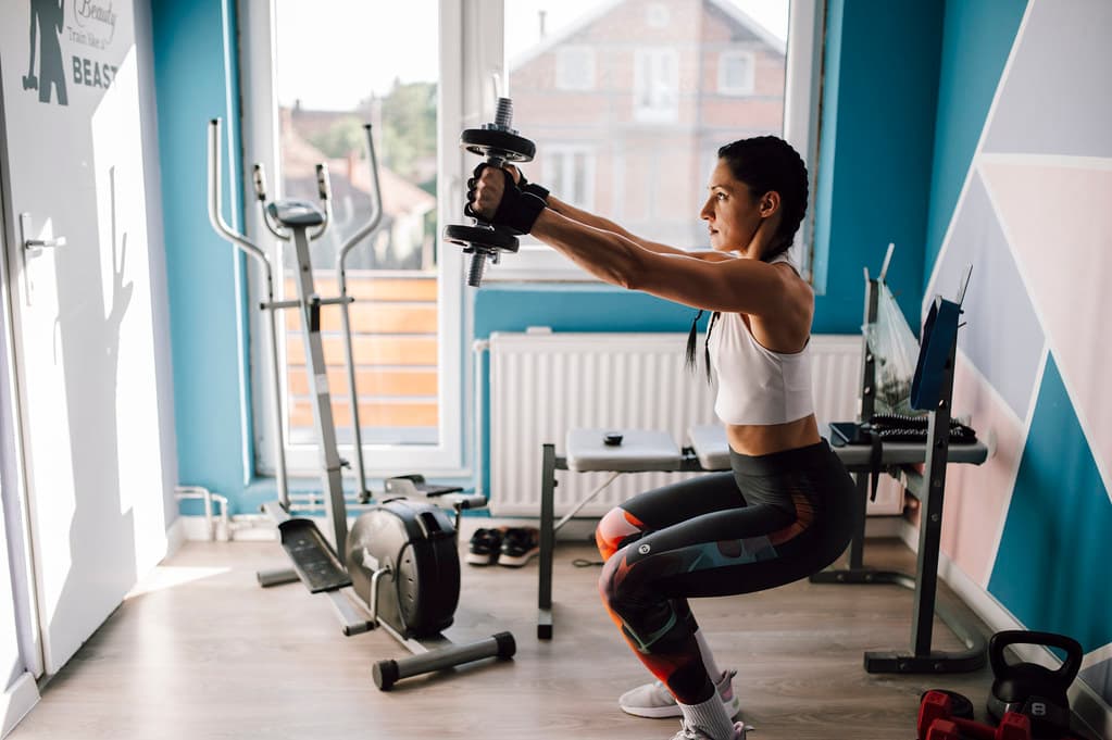 A woman doing a dumbbell squat in a compact home gym